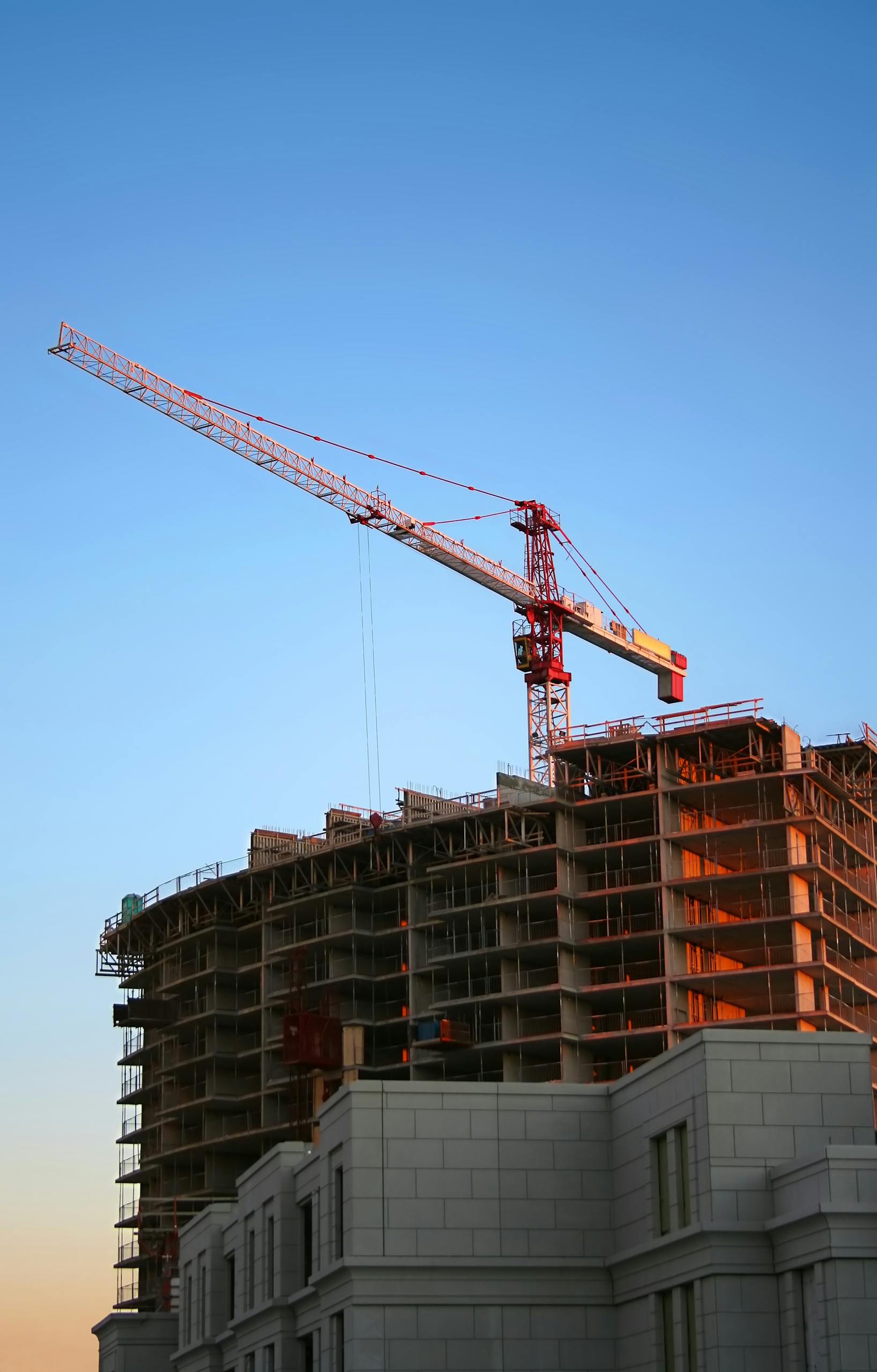 Infrastruktur, Gebäude und Konstruktion 12 laserreinigung infrastruktur Tower crane on a high-rise building under construction at sunset, showcasing modern urban development.
